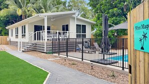 Een gelijkvloers huis met een overdekte veranda, een omheind zwembad en een bordje met de tekst 'Miss Maggie'.