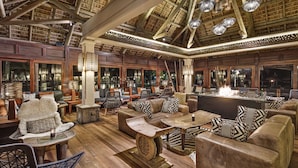 Ein großzügiger Lounge-Bereich mit Holzboden, Ledersofas, gemusterten Kissen und einer zentralen Bar mit Kaminfeuer.