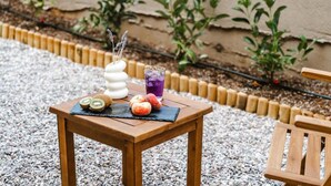 A wooden table with sliced kiwi, peaches, and a drink on a black mat, surrounded by gravel and plants. - Chic Family Villa With Pool in Syvota (Igoumenitsa)