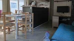 Un ambiente compatto con zona pranzo, angolo cottura e TV a parete.