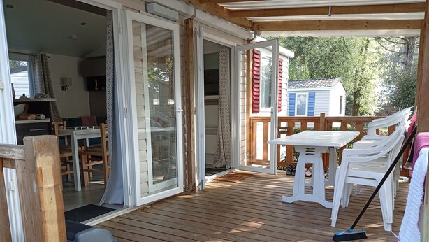 Un terrazzo in legno con tavolo e sedie, un cestino e una porta scorrevole in vetro che dà su un ambiente interno.