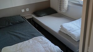 Una stanza piccola e accogliente con due letti singoli, uno scaffale sopra i letti e una finestra con tende decorate.