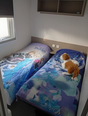 Una cama con dos camas individuales, un edredón con tema de Disney Frozen y una ventana con persianas.