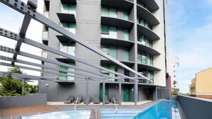 Un edificio moderno con piscina en la azotea, balcones y cielo despejado.