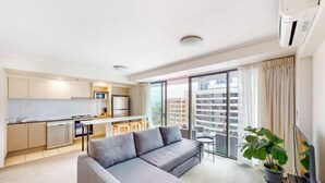 A modern apartment with a kitchenette, a grey sofa, a small dining table, and a balcony with a view of the city. - River and city view 1 Bedroom apartment (Brisbane City)