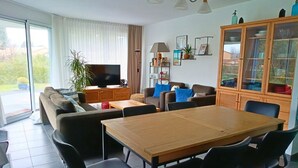 Una sala de estar moderna con un sofá, televisor, mueble de madera y una mesa de comedor con sillas.