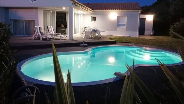 Una casa con piscina, un patio cubierto con sillones de descanso y un garaje.