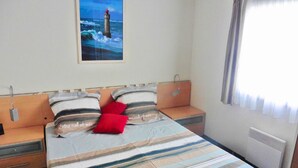 Una cama con ropa de cama a rayas, dos almohadas, una mesita de noche, una lámpara de pared y un cuadro de un faro.