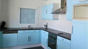 Una cocina con armarios azul claro, encimera negra, ventana con persianas, cafetera y estufa.