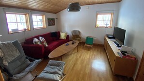 Un salón con techo de madera, un sofá rojo, un sillón gris, una mesita y un televisor sobre un mueble de madera.