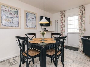 Un comedor con una mesa redonda, cuatro sillas, un florero con flores y dos cuadros en la pared.