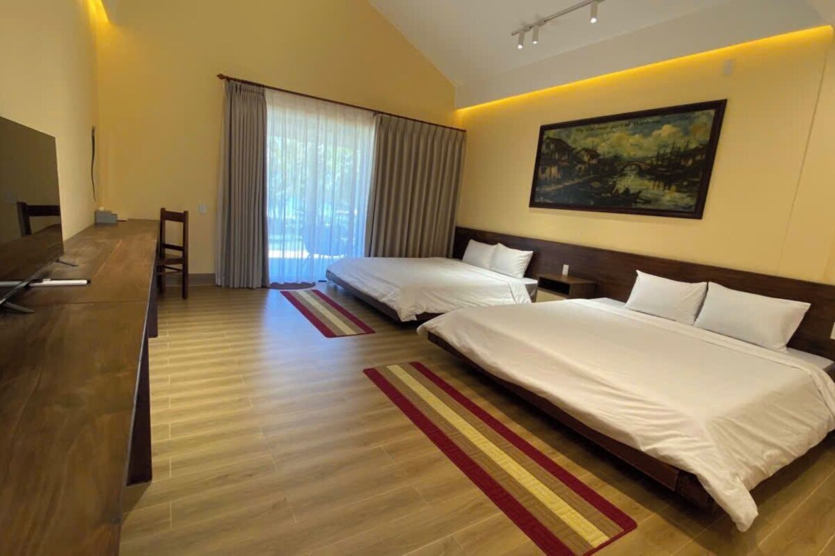 A hotel room with two beds, a TV, a desk, and a large window with curtains.
