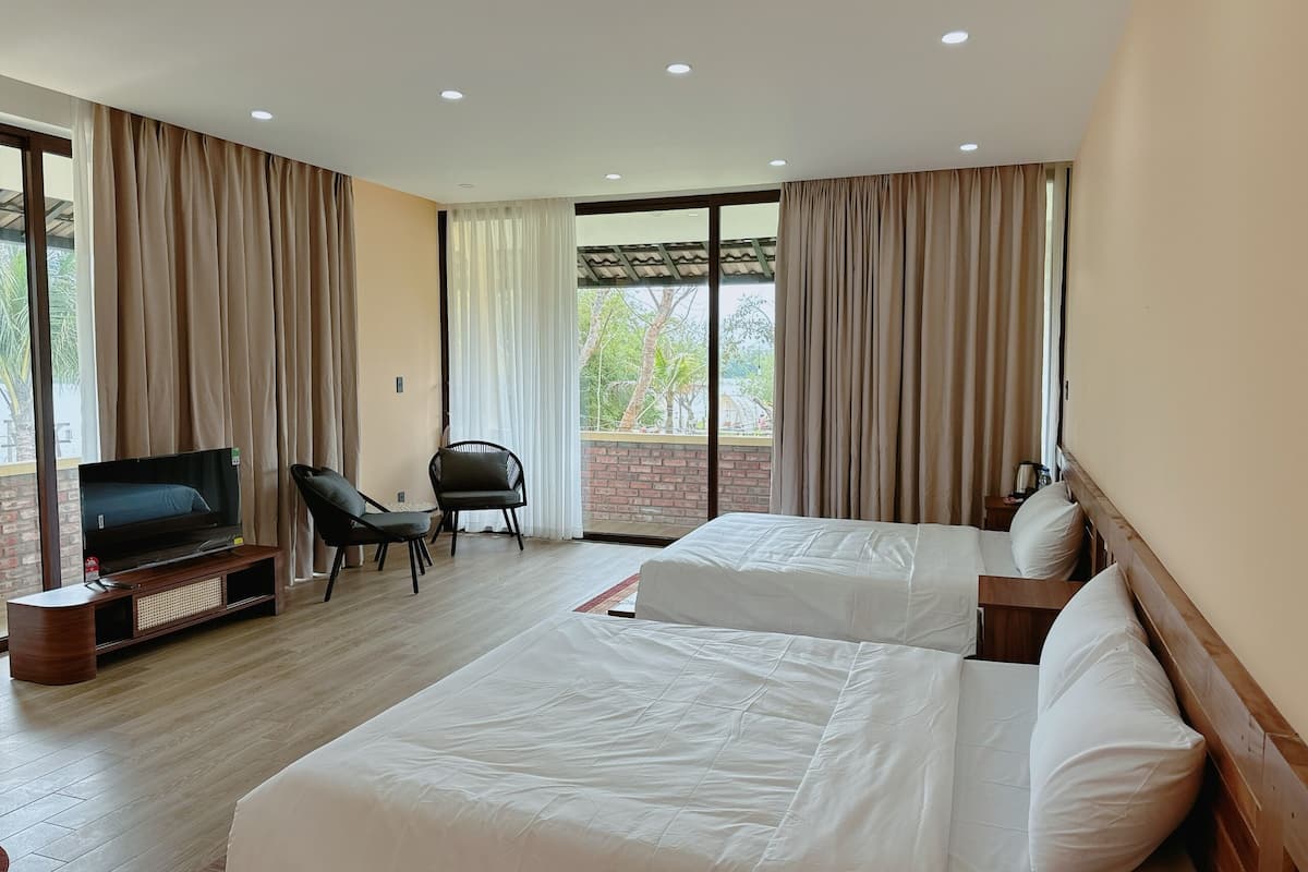 Quarto de hotel com duas camas, televisão, uma cadeira e varanda com vista.
