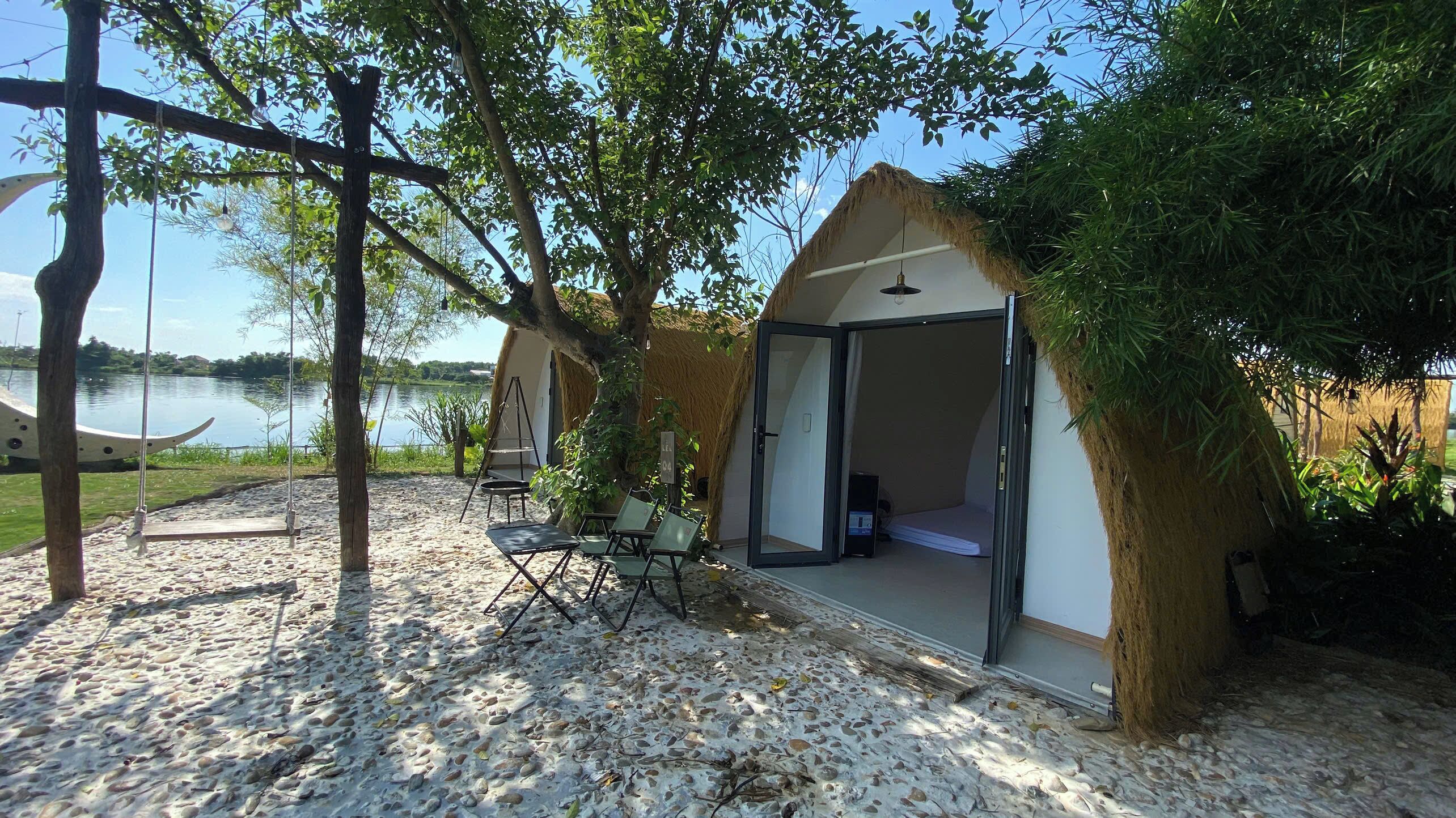 Estructura con techo de paja que ofrece vista a un lago, con asientos al aire libre y un columpio.