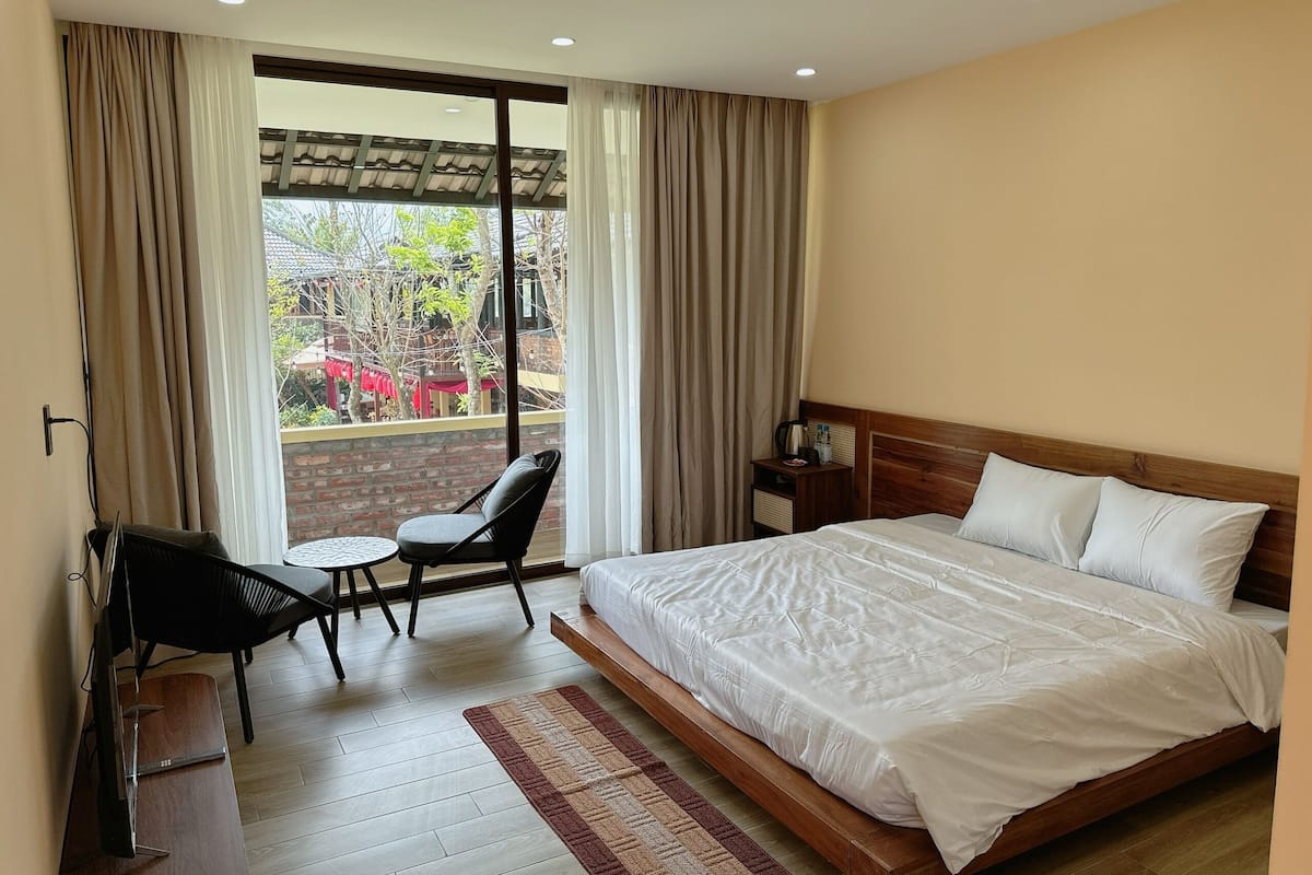 Quarto de hotel com cama, televisão, pequena mesa com cadeira e vista para o exterior.