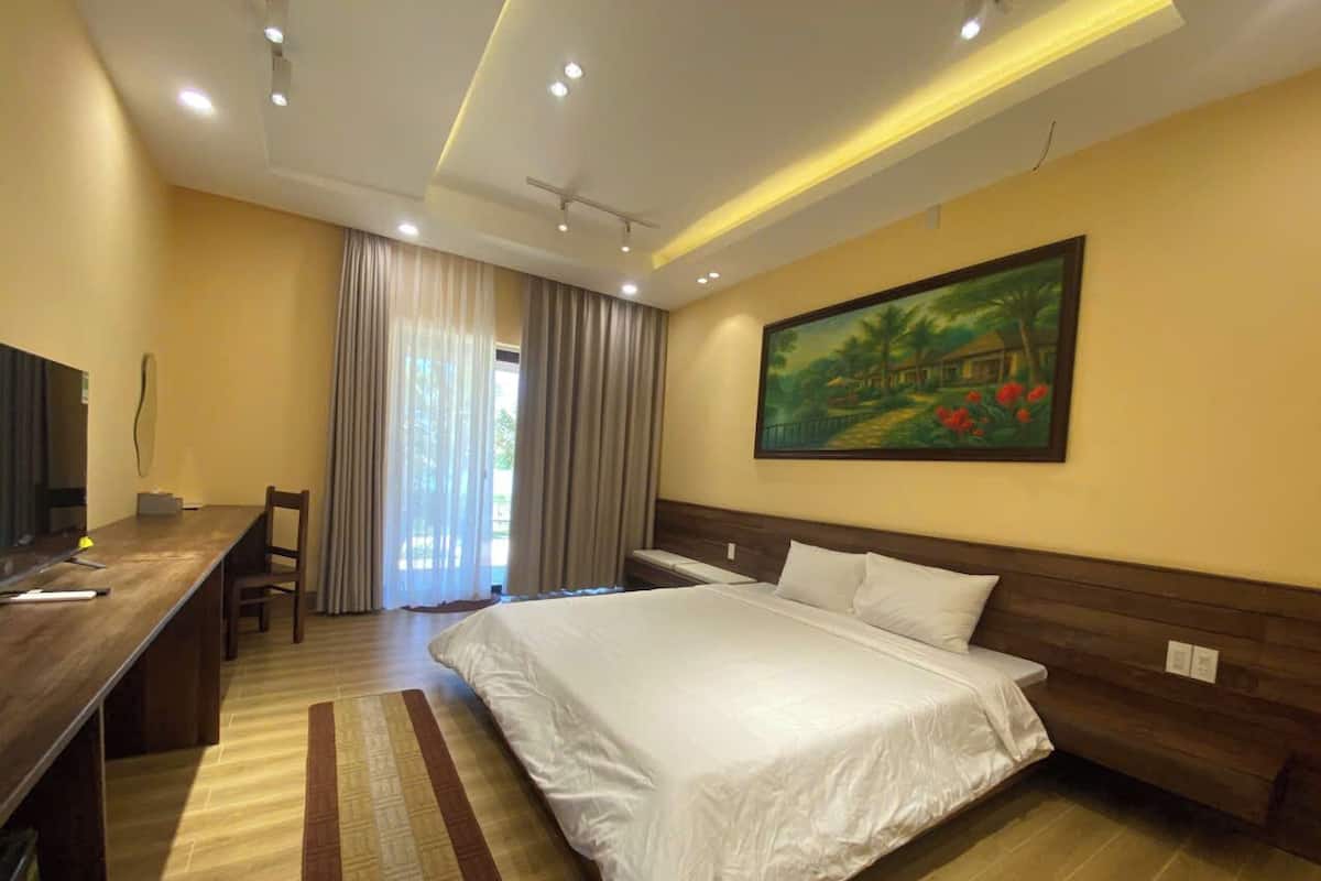 Quarto de hotel com cama, escrivaninha, cadeira, um quadro e vista para o exterior.