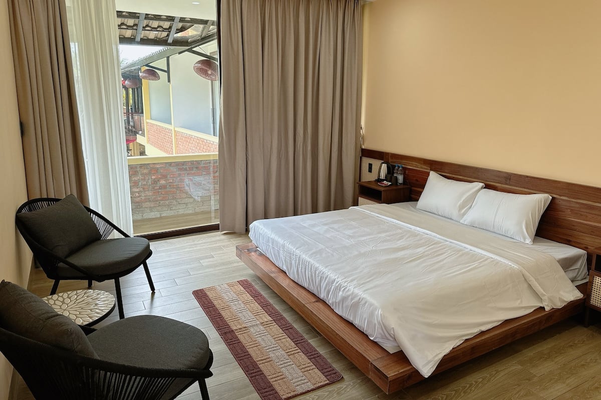Quarto de hotel com cama, uma cadeira, mesa de cabeceira e vista para uma varanda.