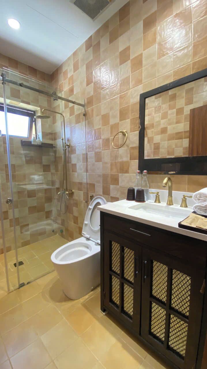 A bathroom with a glass-enclosed shower, a toilet, a sink with a mirror, and a cabinet with a towel rack.