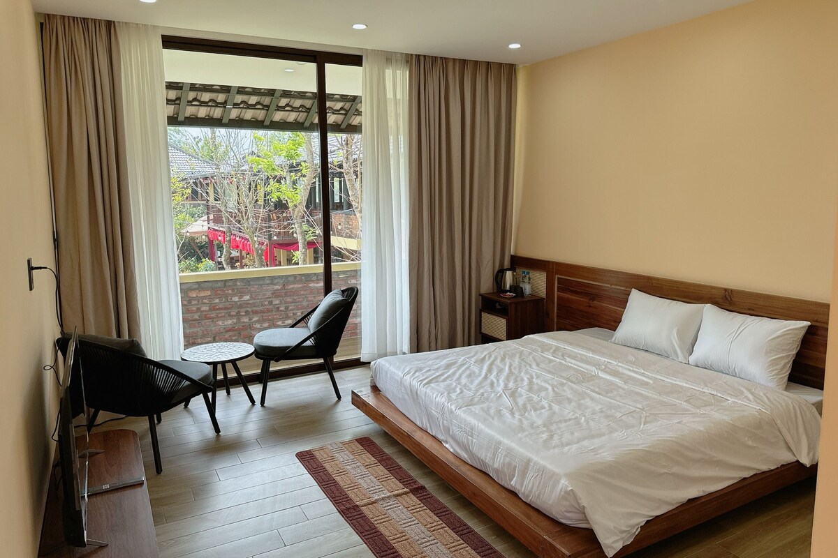 A hotel room with a bed, a TV, a small table with a chair, and a view of the outside.