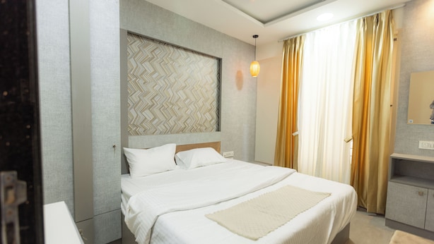 A hotel room with a large bed, a headboard with a geometric pattern, a bedside table, and a mirror on the wall. - SUNIQ (Bengaluru)