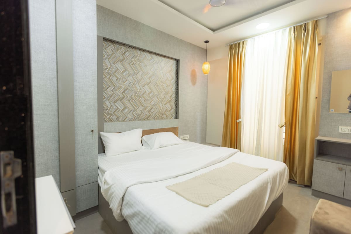 A hotel room with a large bed, a headboard with a geometric pattern, a bedside table, and a mirror on the wall.