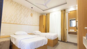 A hotel room with three single beds, a wooden wardrobe, a ceiling fan, and a bathroom with a mirror and sink. - SUNIQ (Bengaluru)