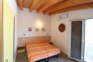 Ein Schlafzimmer mit einem Bett, einem Nachttisch, einer Wandleuchte, einem Fenster mit Blick und einer Tür mit einer Fliegengitter.