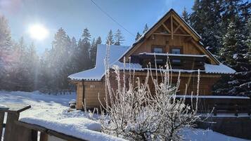 Una cabaña de madera con techo inclinado, rodeada de árboles cubiertos de nieve.