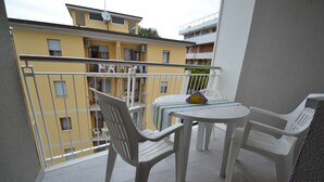 En balkon med hvide plastikstole og et bord, der ud til et gult hus med flere balkoner.