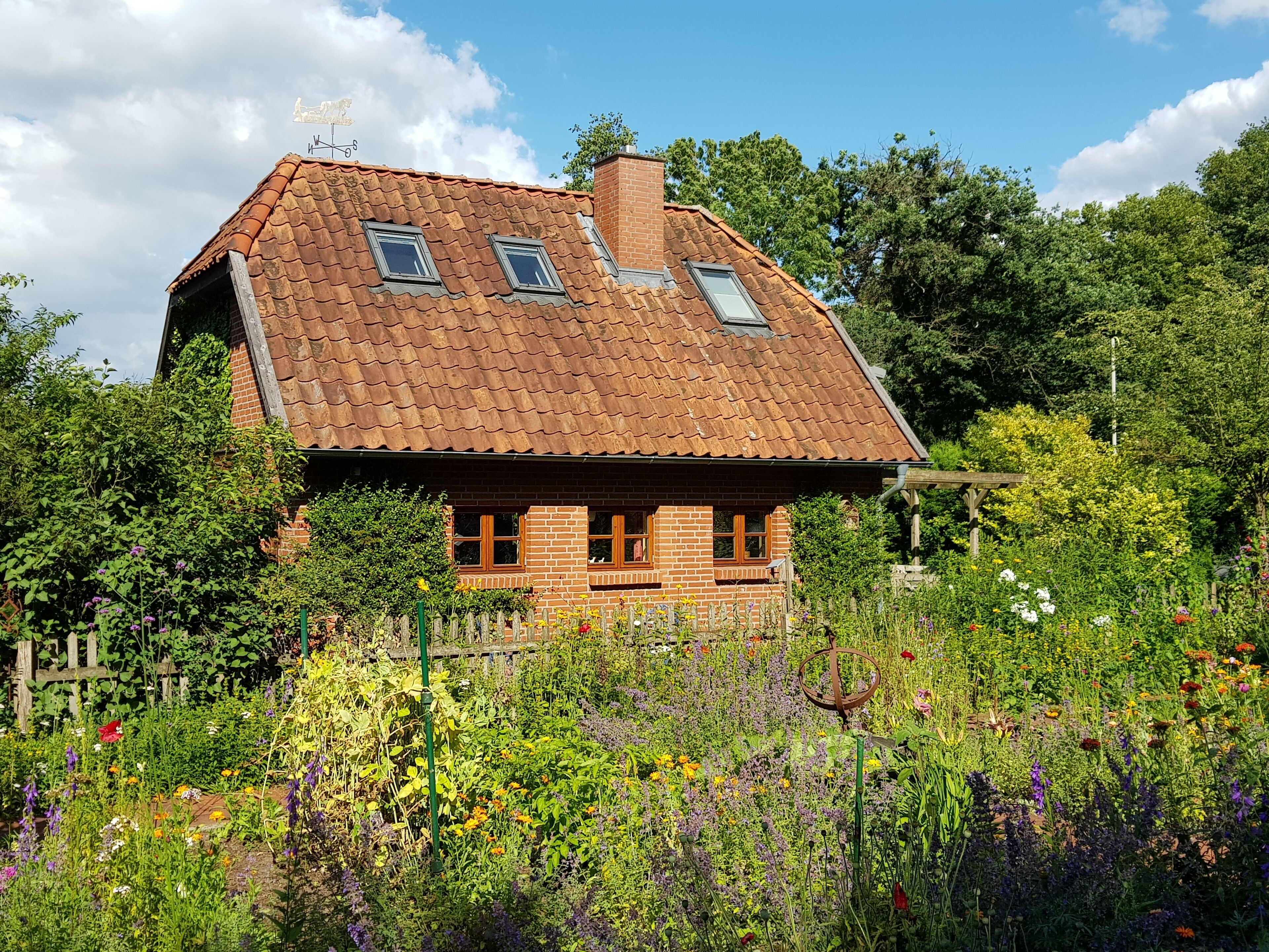 Een landelijk huis met schuin dak, bakstenen muren en een tuin vol verschillende bloemen.