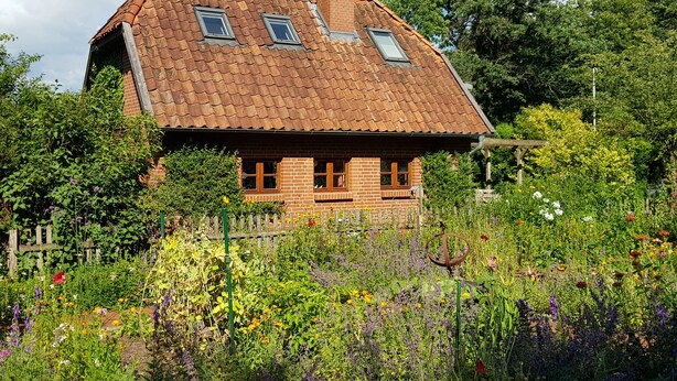 Een landelijk huis met schuin dak, bakstenen muren en een tuin vol verschillende bloemen.