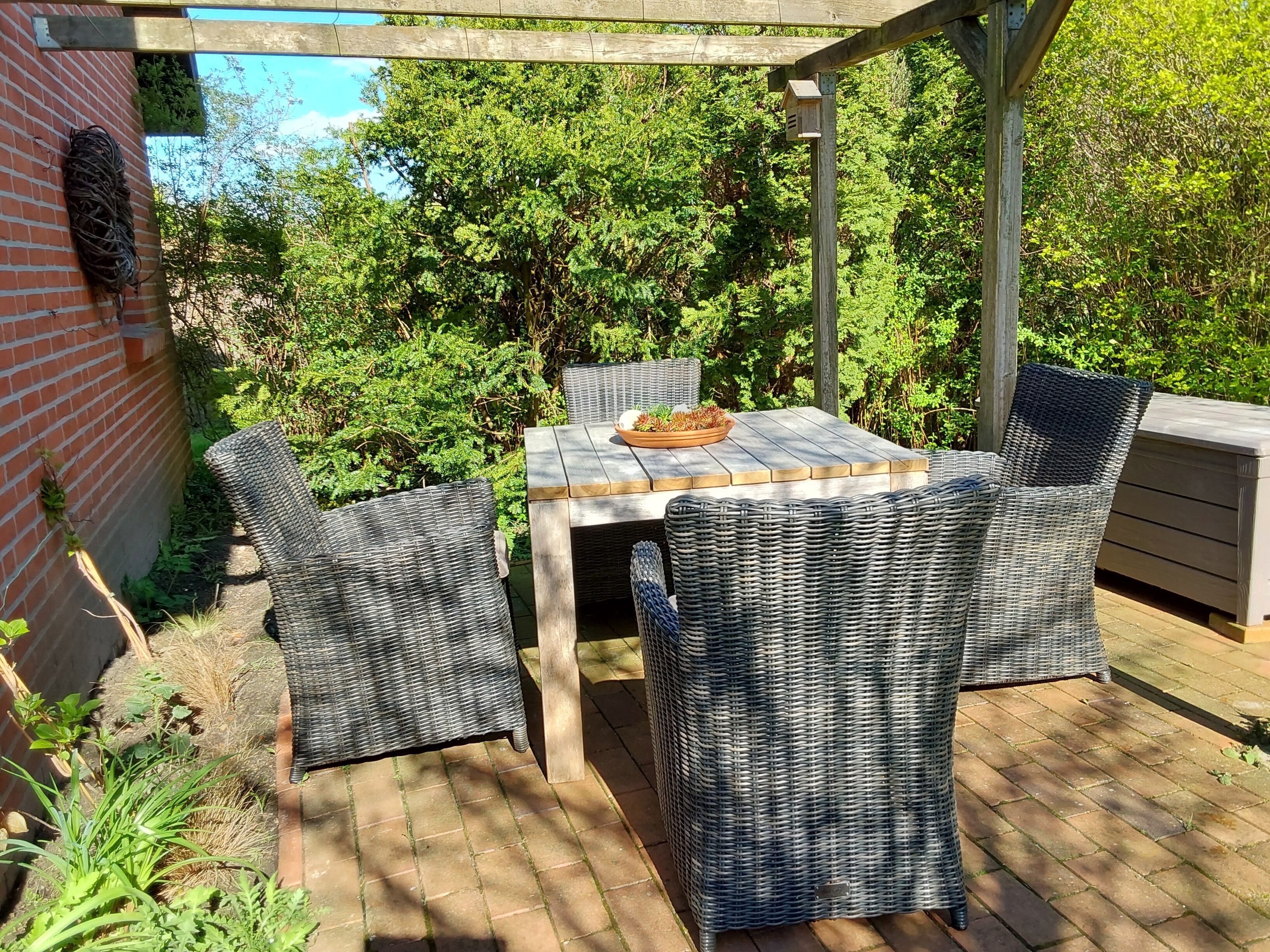 Eine Terrasse im Freien mit Korbmöbeln, einem Holztisch und einer Backsteinmauer.
