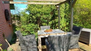 Een terras buiten met rieten meubels, een houten tafel en een bakstenen muur.
