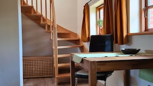 Een kamer met een houten trap, een tafel met stoel, een hanglamp en een raam met gordijnen.