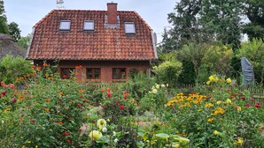 Een huis met een rode pannendak, een bakstenen gevel en een tuin vol met verschillende bloemen.