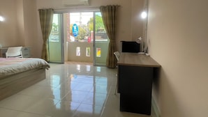 A bedroom with a bed, a desk, a chair, a window with curtains, and an air conditioning unit. - Rawai cozy hostel (Rawai)