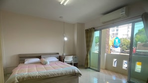 A bedroom with a bed, a desk, a chair, and a sliding glass door to a balcony. - Rawai cozy hostel (Rawai)