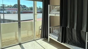 A room with a bunk bed, an air conditioning unit, a sliding glass door, and a view of buildings outside. - Rawai cozy hostel (Rawai)