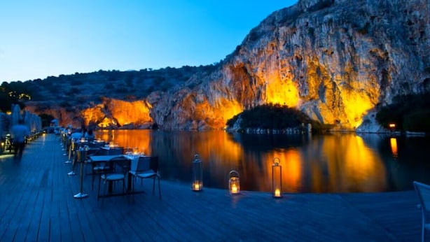 A waterfront restaurant with outdoor seating, a rocky cliff, and a calm body of water. - Luxury Boutique Apartment • 5-Minute Walk to the Beach • Athens Riviera (Vouliagmeni)