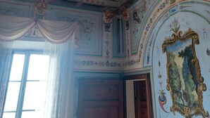 Una habitación con elaborados adornos en el techo, un ventanal con cortinas y una puerta de madera.