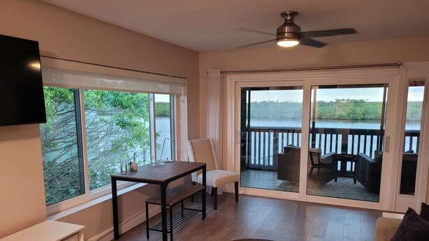 A room with a TV, a table, a sofa, and a balcony with a view of the water. - Bahia Del Sol Condo (Ruskin)
