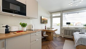 Eine moderne Küche mit einer Bosch-Mikrowelle, einer Kaffeemaschine und einem Toaster. Es gibt eine Essecke mit Tisch und Stühlen sowie ein Bett mit weißer Decke.