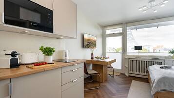 A modern kitchen with a Bosch microwave, a coffee maker, and a toaster. There is a dining area with a table and chairs, and a bed with a white blanket.