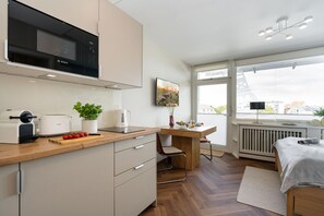 Eine moderne Küche mit einer Bosch-Mikrowelle, einer Kaffeemaschine und einem Toaster. Es gibt eine Essecke mit Tisch und Stühlen sowie ein Bett mit weißer Decke.