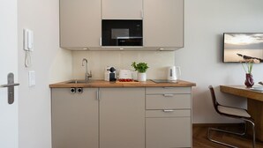 Eine kompakte Küche mit einer Mikrowelle, einem Toaster und einer Kaffeemaschine auf der Arbeitsplatte, einem Spülbecken und einem Stuhl.