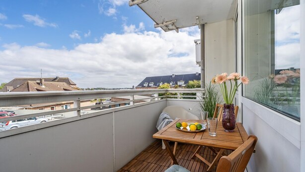 Ein Balkon mit einem Holztisch, einer Blumenvase und Blick auf Gebäude und Autos.
