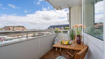 Ein Balkon mit einem Holztisch, einer Blumenvase und Blick auf Gebäude und Autos.