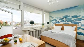 A hotel room with a bed, a dining table with plates and glasses, a window with a view of buildings, and a wall with a blue whale mural.