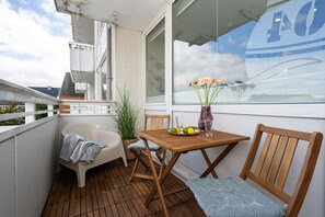 A balcony with a wooden table, a chair, a small potted plant, a vase with flowers, and a bathtub. - Boje - Modern, centrally located apartment with a balcony, parking, and Wi-Fi. Pets Allowed (Sylt)