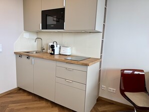 A kitchenette with a microwave, toaster, and coffee maker on a wooden countertop, a sink, and a red chair. - Boje - Modern and central app. with balcony, parking space, WLAN. Pets (Sylt)